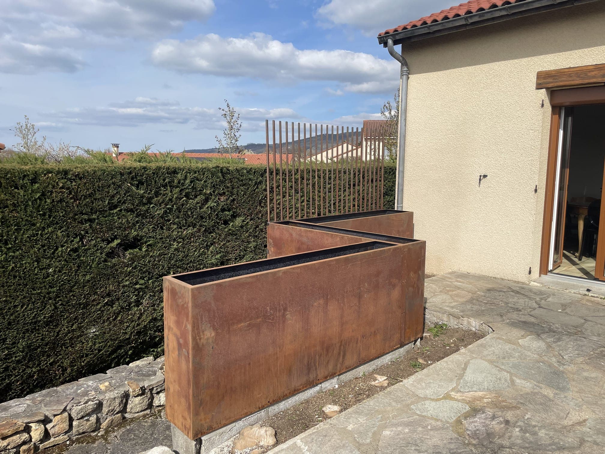Vue depuis la terrasse des bacs en Corten assemblés à angle droit, haie et claustra en arrière-plan