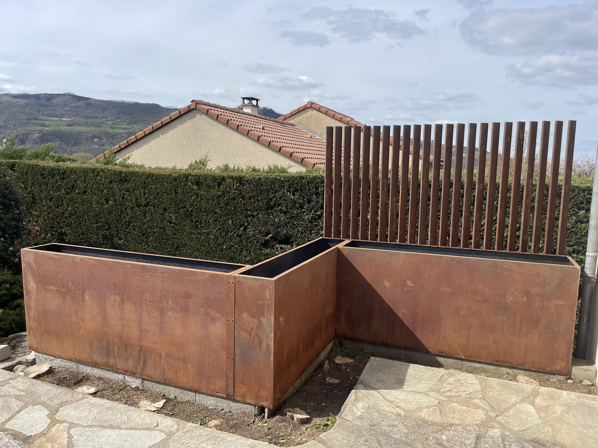 Bac à fleurs en acier Corten en bordure de terrasse, surmonté d’un claustra de lames verticales
