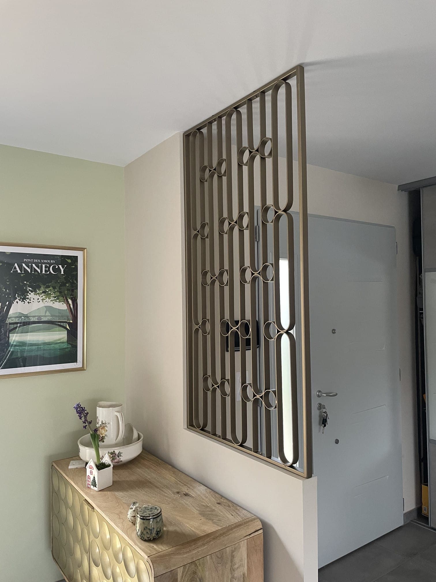 Claustra Art déco teinte bronze posé entre un muret et le plafond, à côté d’une porte d’entrée