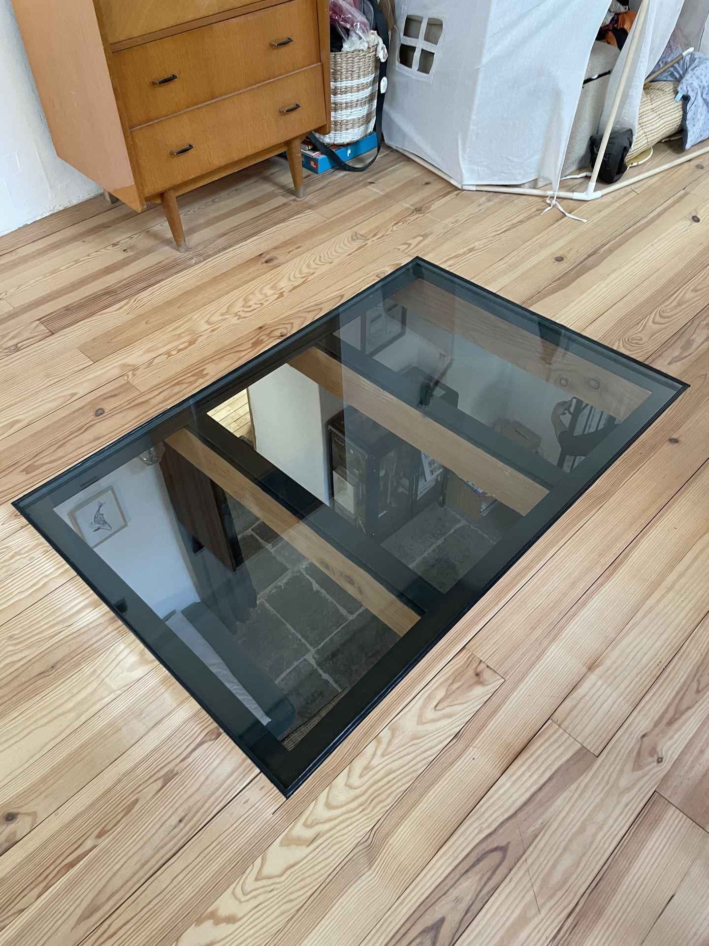 Dalle de sol vitrée à cadre noir intégrée dans un parquet clair, vue en plongée sur la pièce du dessous