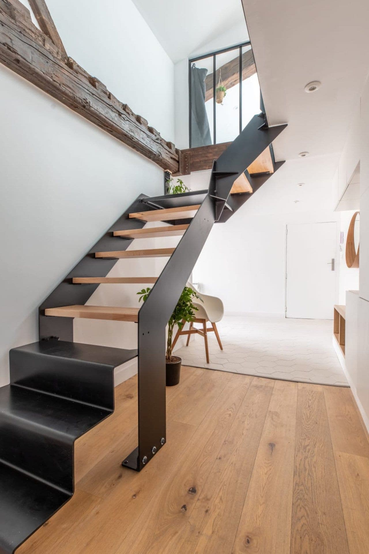 Escalier acier noir et bois clair vu de trois quarts : trois marches basses en acier plié, volée en bois, palier haut