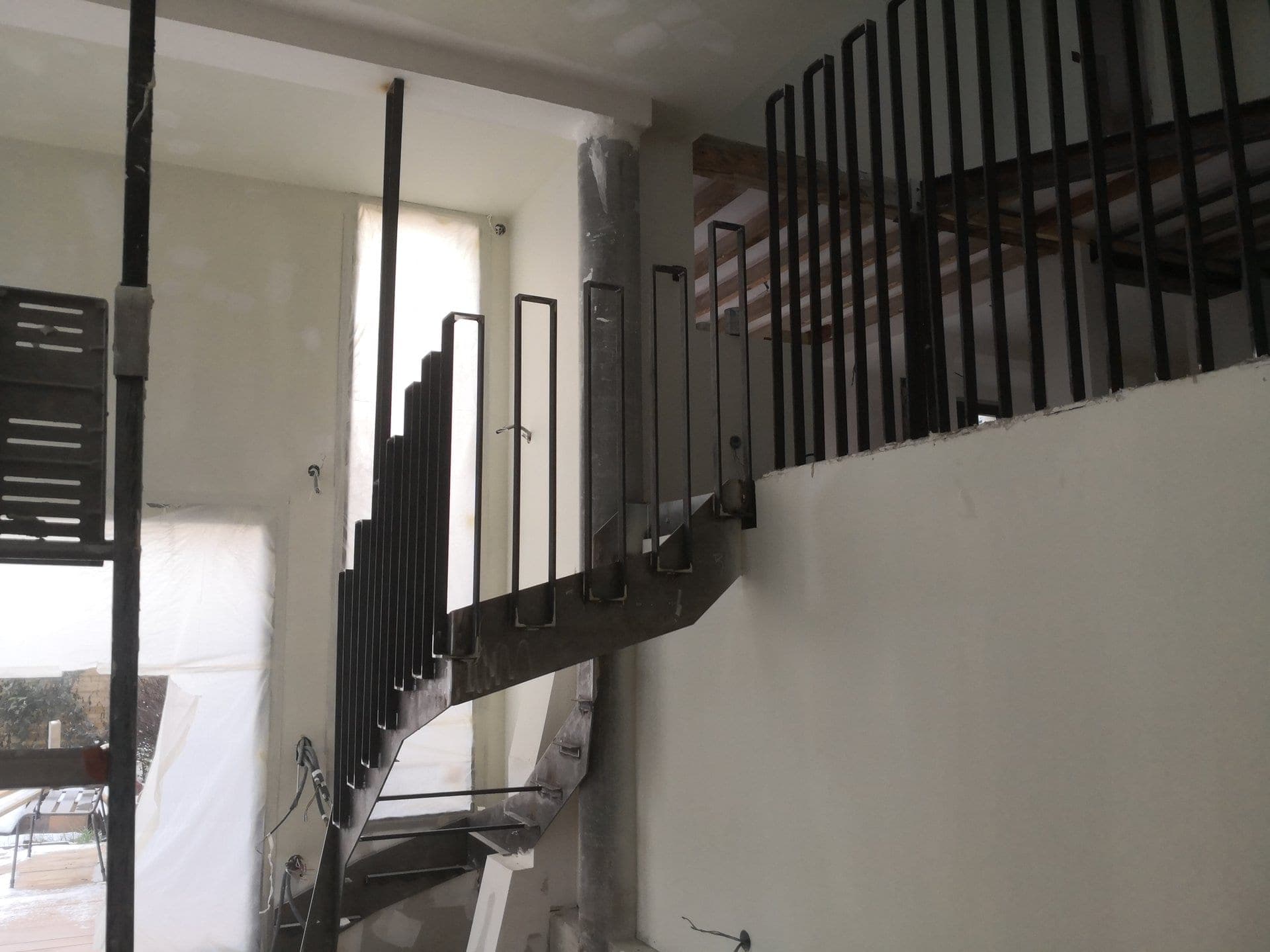 Vue d’ensemble de l’escalier en acier autour du poteau en béton, garde-corps du palier au fond