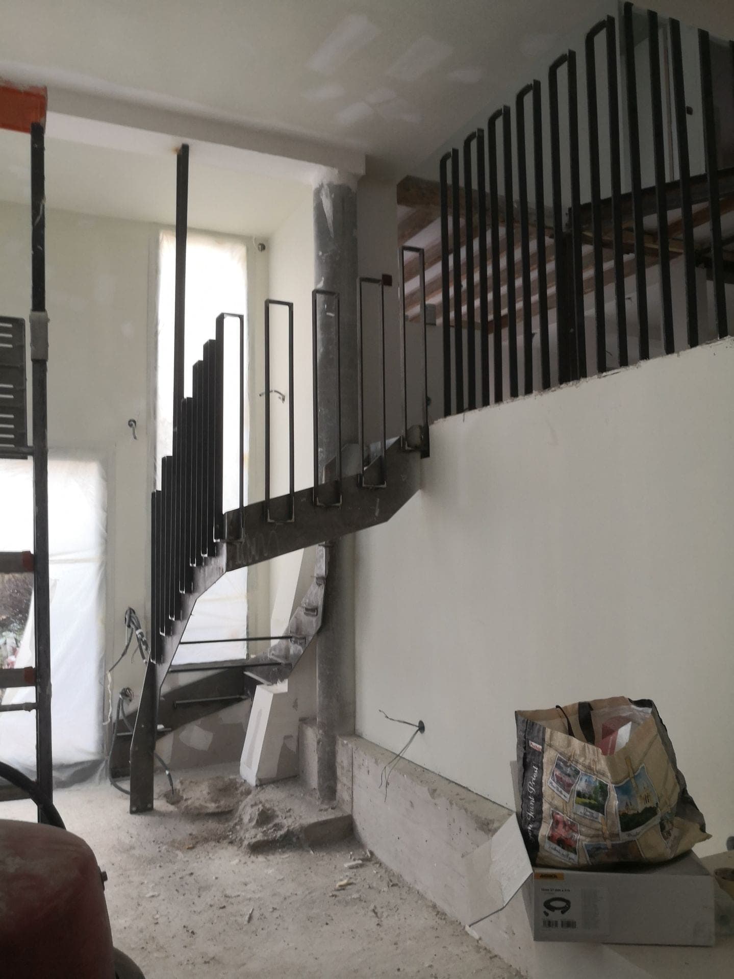 Escalier en acier vu du bas en cours de chantier, palier haut et poutres apparentes