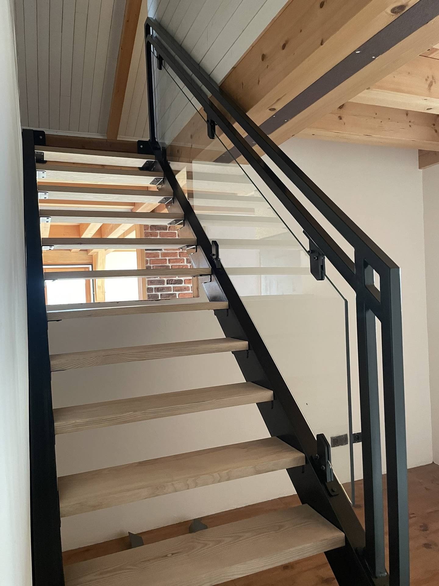 Escalier vu du bas : marches en chêne entre les limons, garde-corps en verre et acier noir, arrivée à l’étage