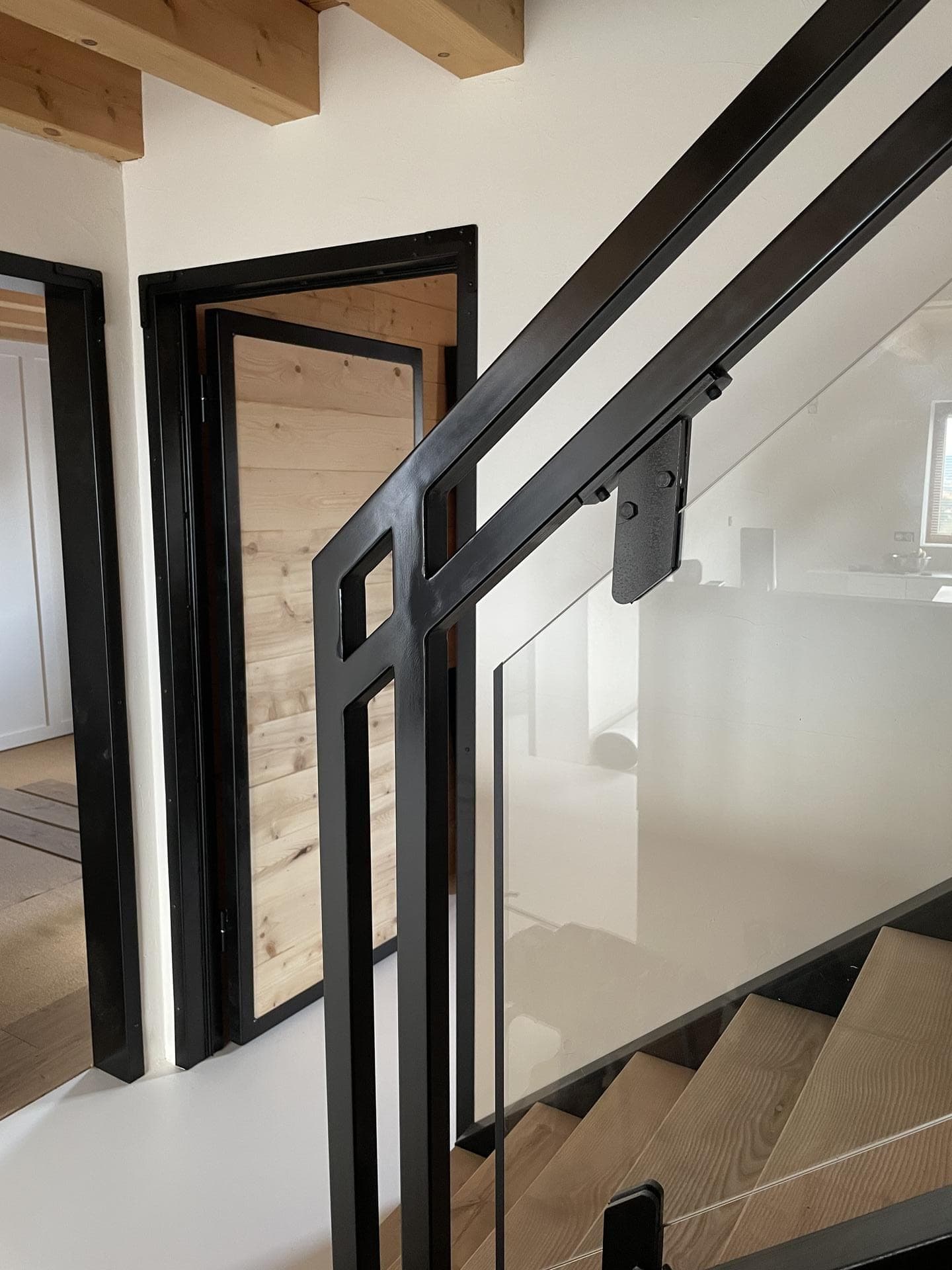 Détail du garde-corps en haut de l’escalier : main courante, montant ajouré et verre tenu par des pinces noires