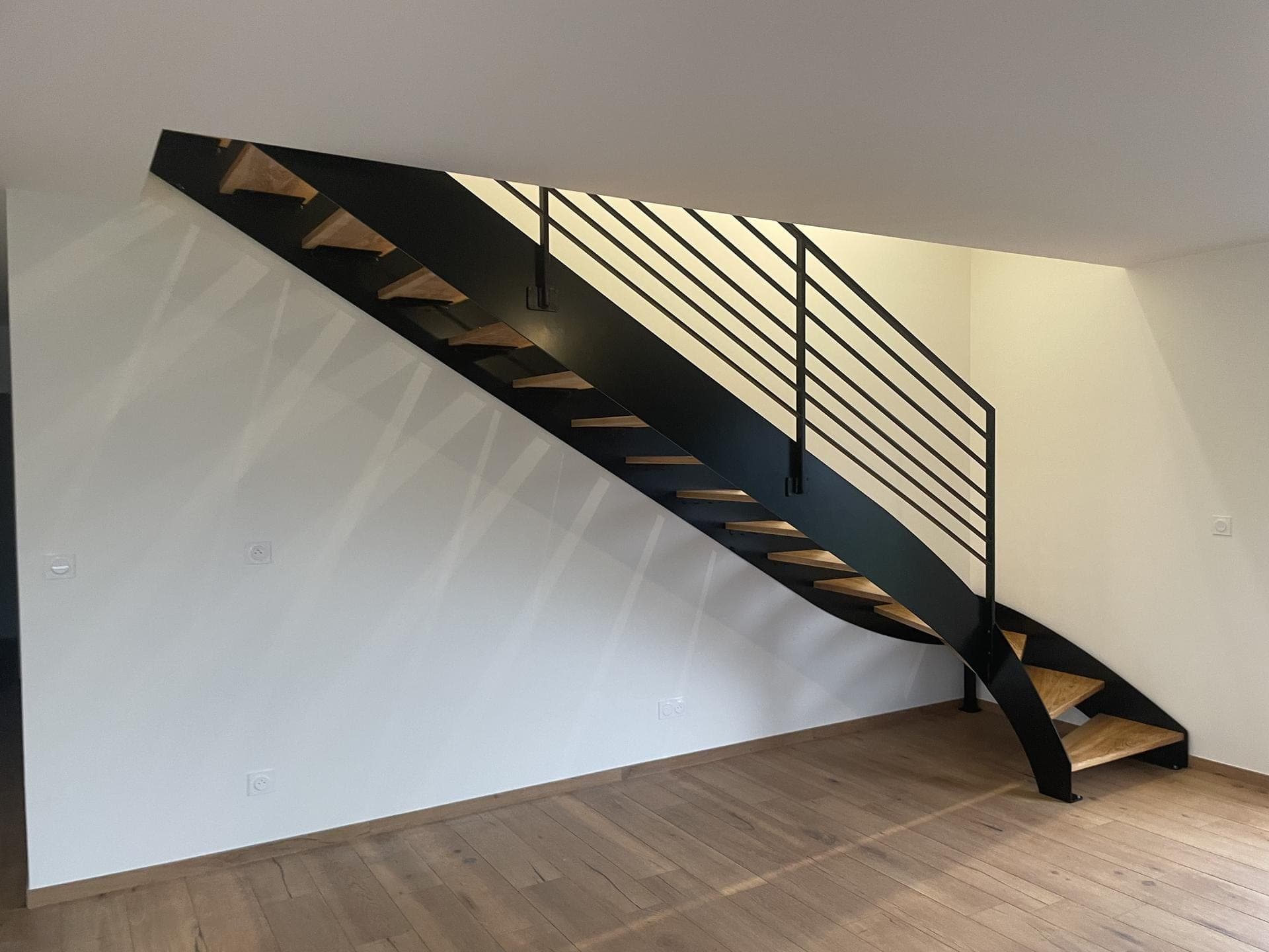Vue d’ensemble de l’escalier : limons en acier noir, marches en frêne, garde-corps à lisses horizontales