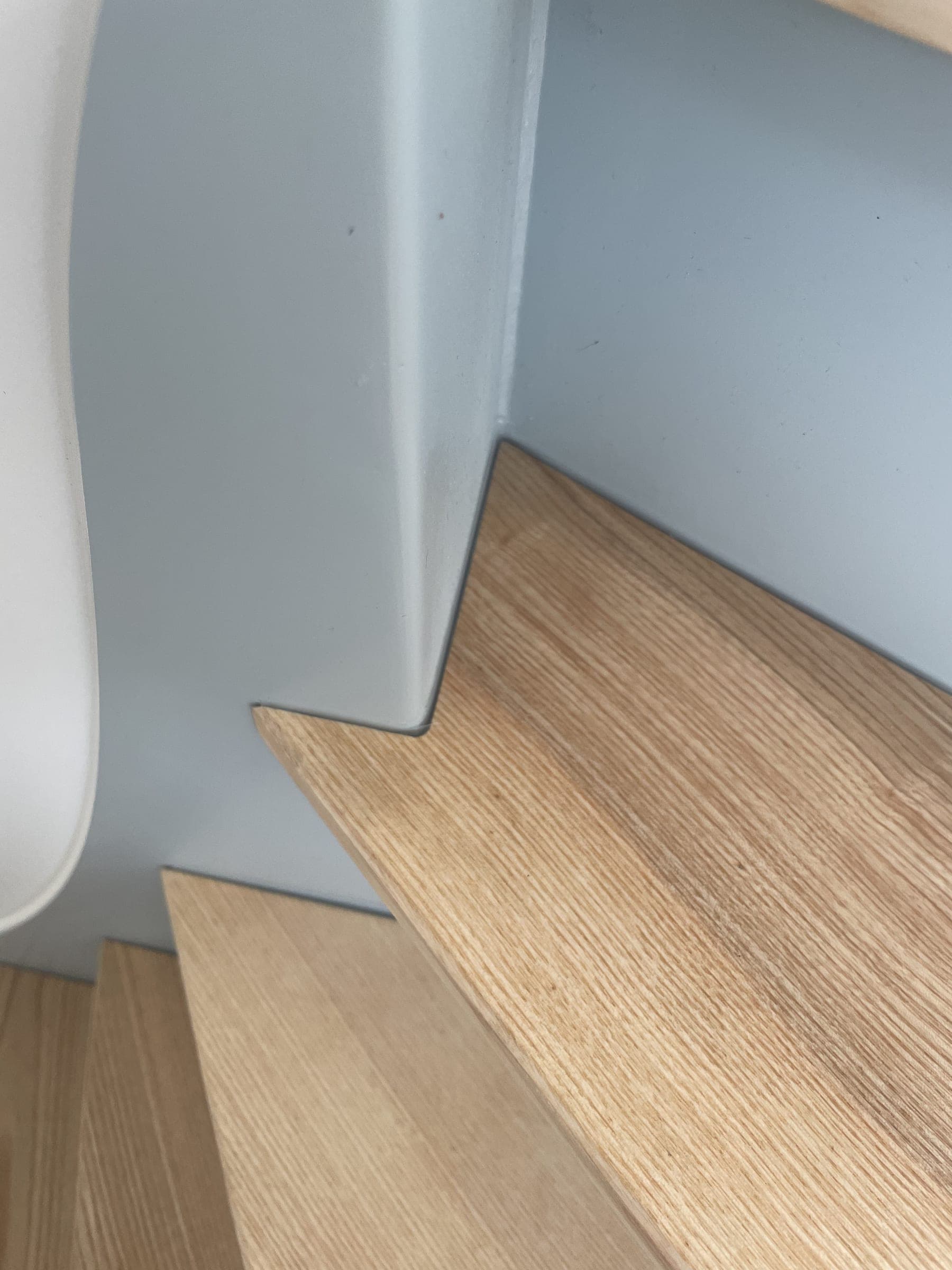 Détail d’une marche en frêne découpée au ras du limon en acier peint gris-bleu