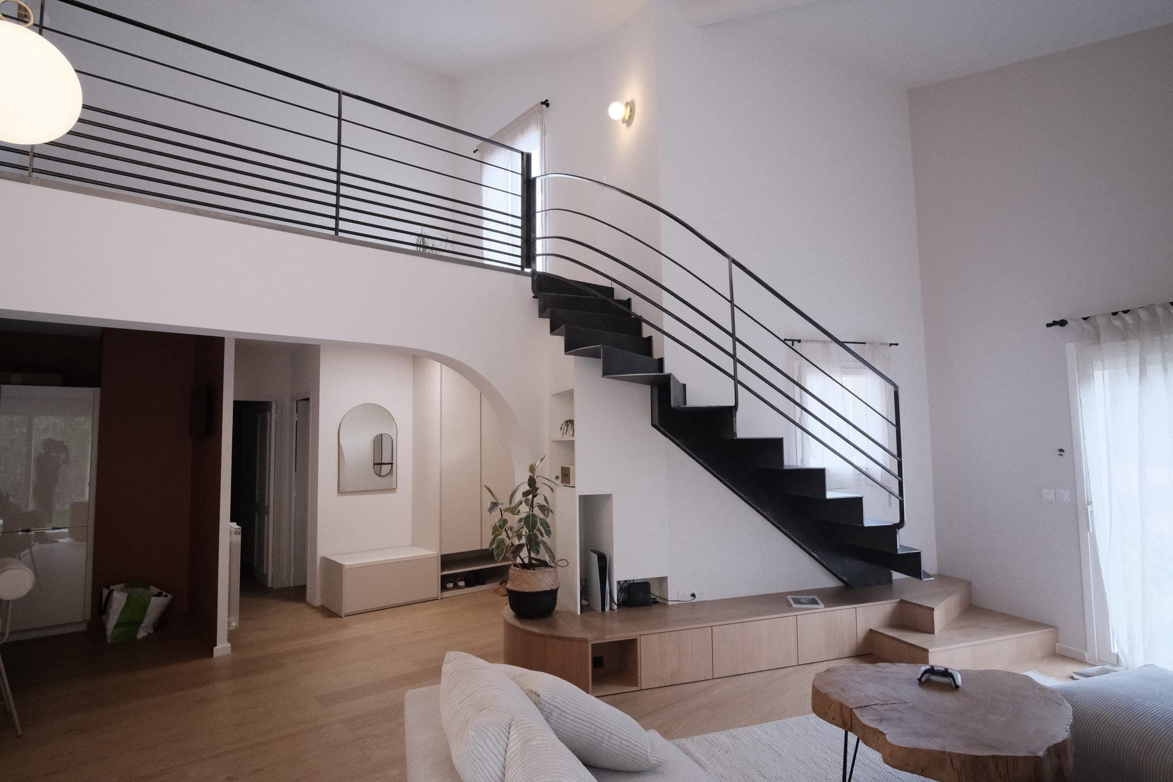 Séjour en double hauteur avec l’escalier en acier brut et son garde-corps prolongé le long de la mezzanine