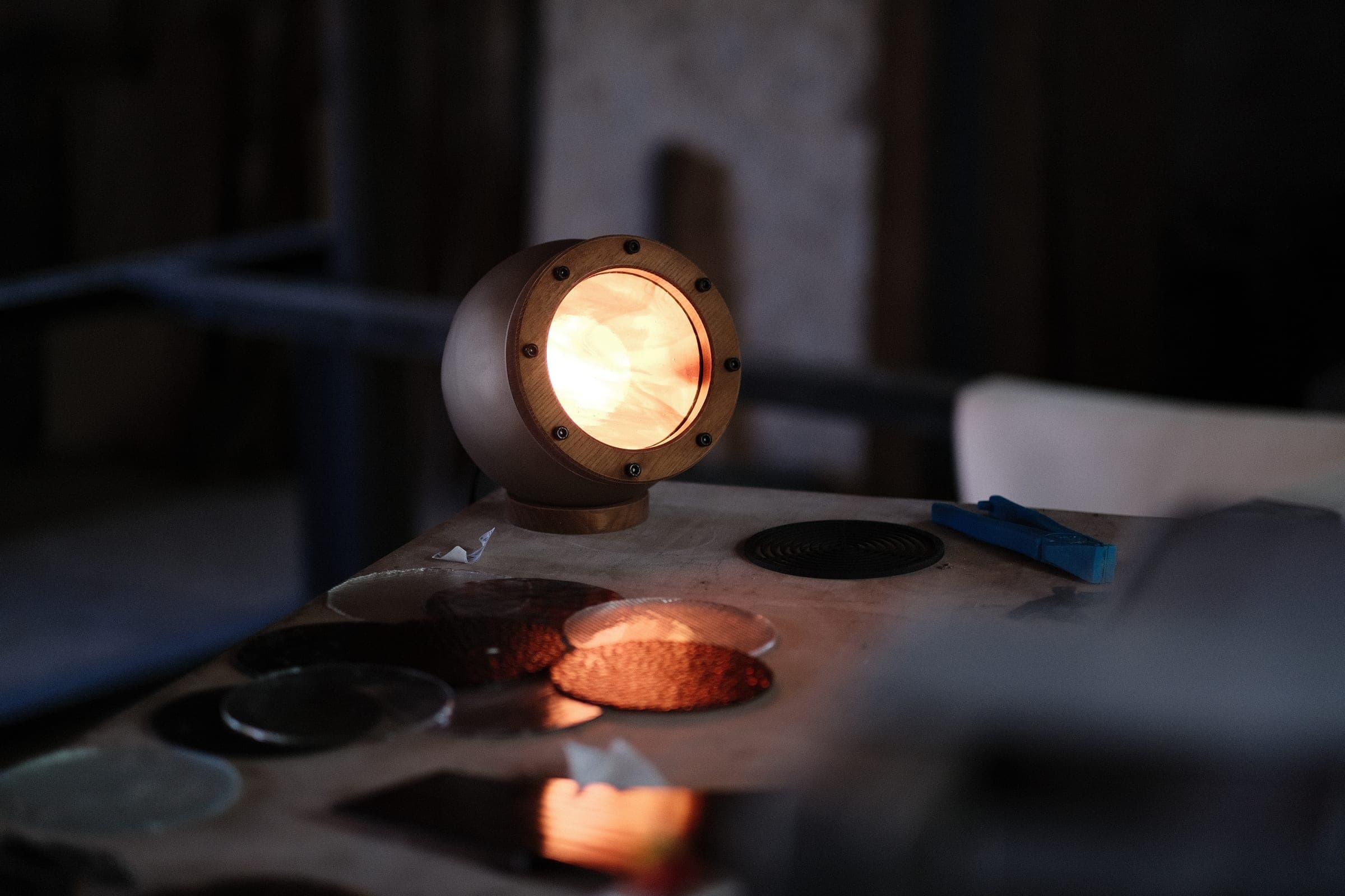 Lampe Abysse allumée dans la pénombre de l’atelier, disques de verre au premier plan