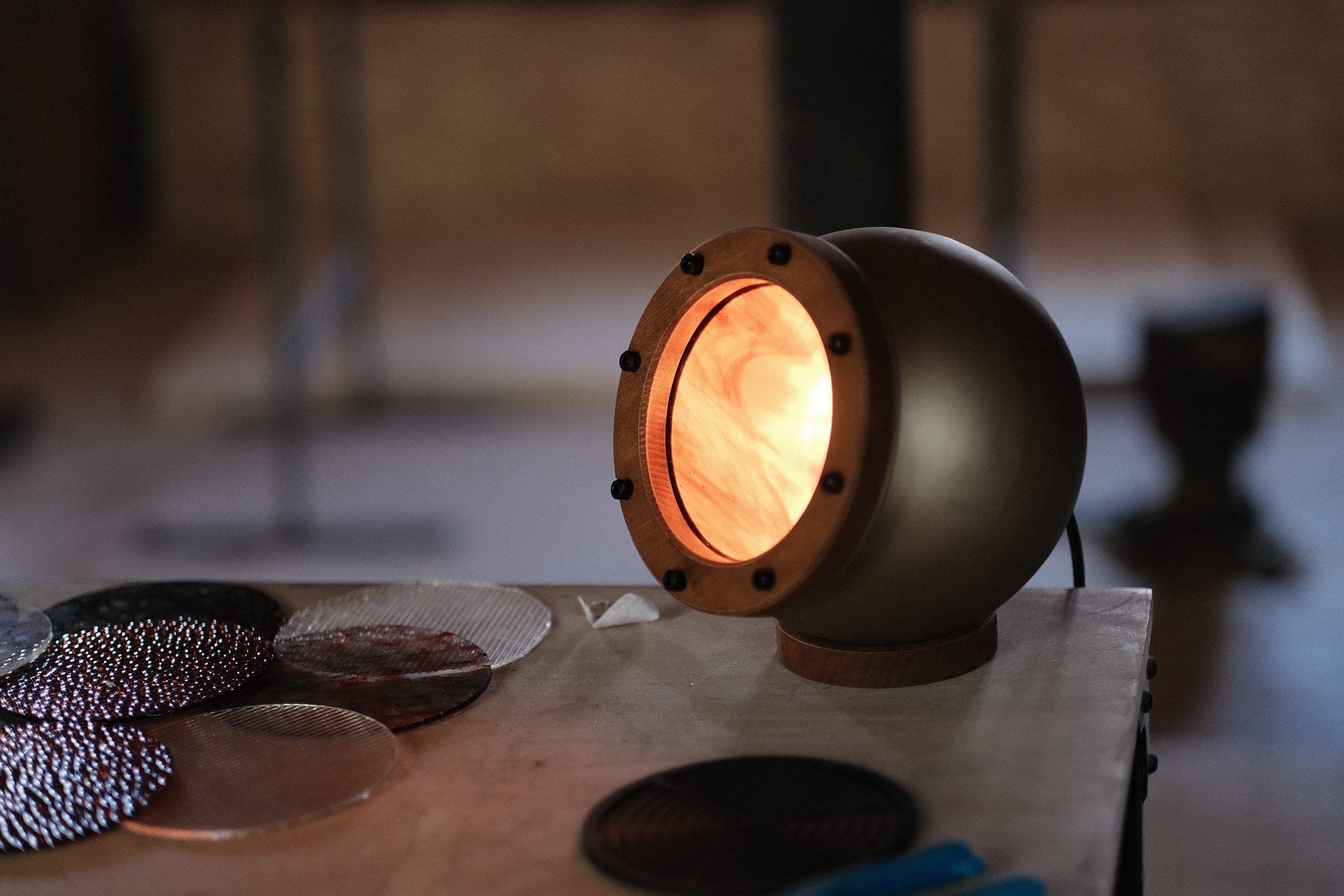 Lampe Abysse allumée sur l’établi, disques de verre texturés posés au premier plan