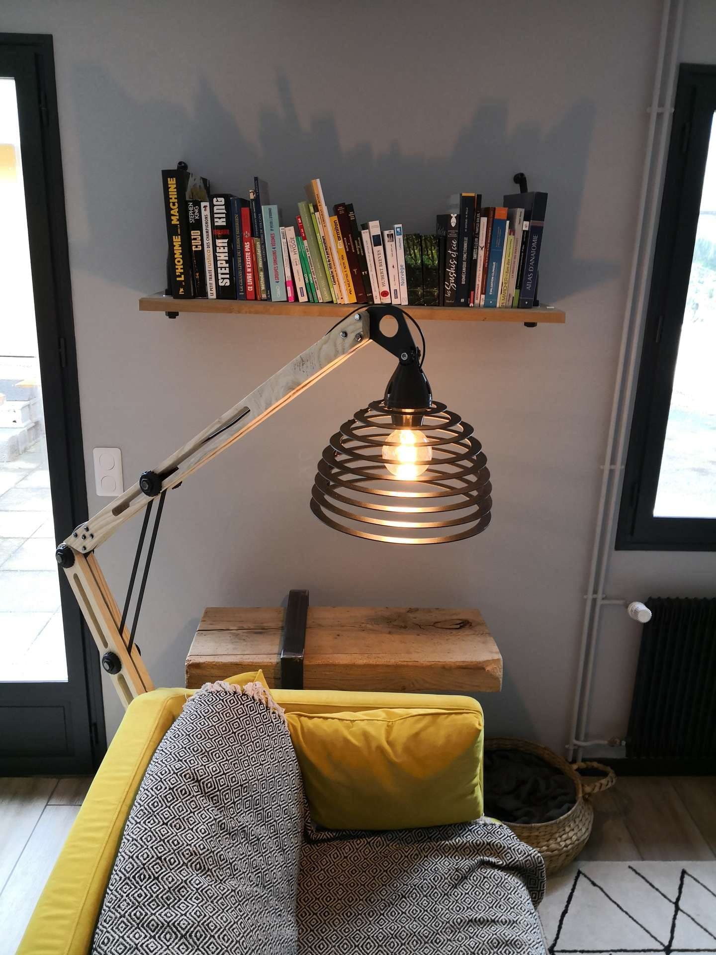 Lampadaire d’architecte en bois et métal déployé au-dessus d’un canapé jaune, ampoule allumée