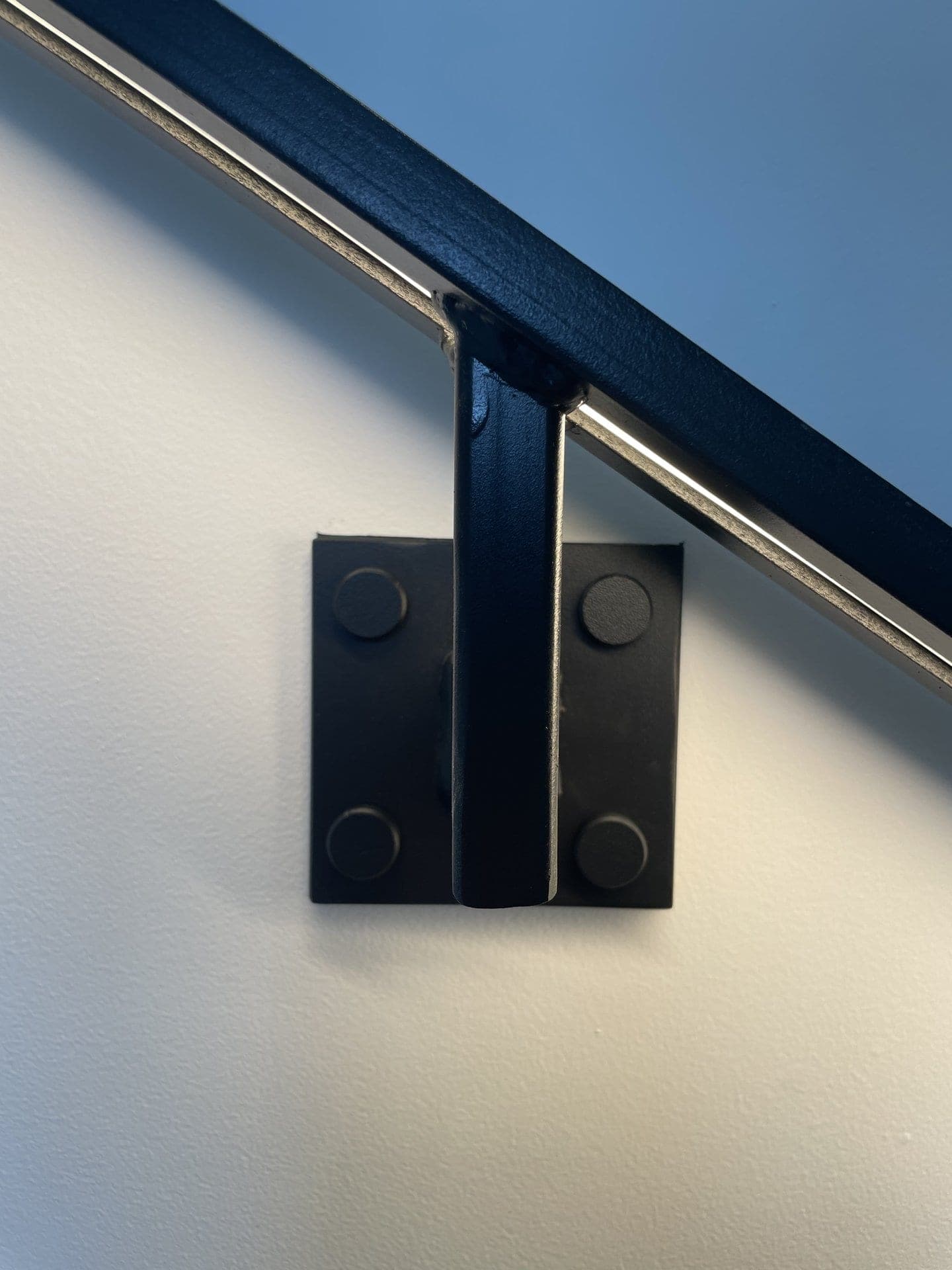 Détail d’une fixation murale : platine carrée à quatre points et patte en acier sous le plat