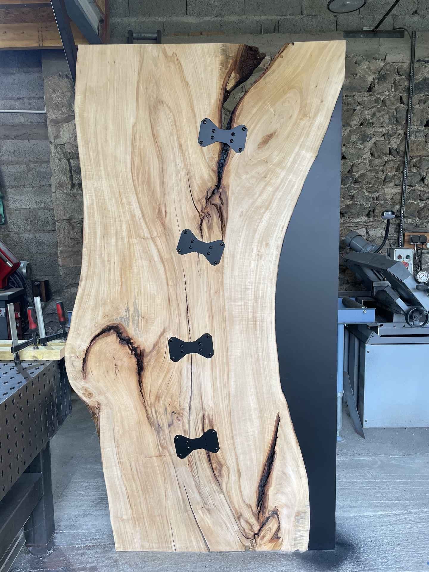 Porte en tilleul massif vue de face : bord naturel, insert en métal noir et quatre papillons vissés sur la fente
