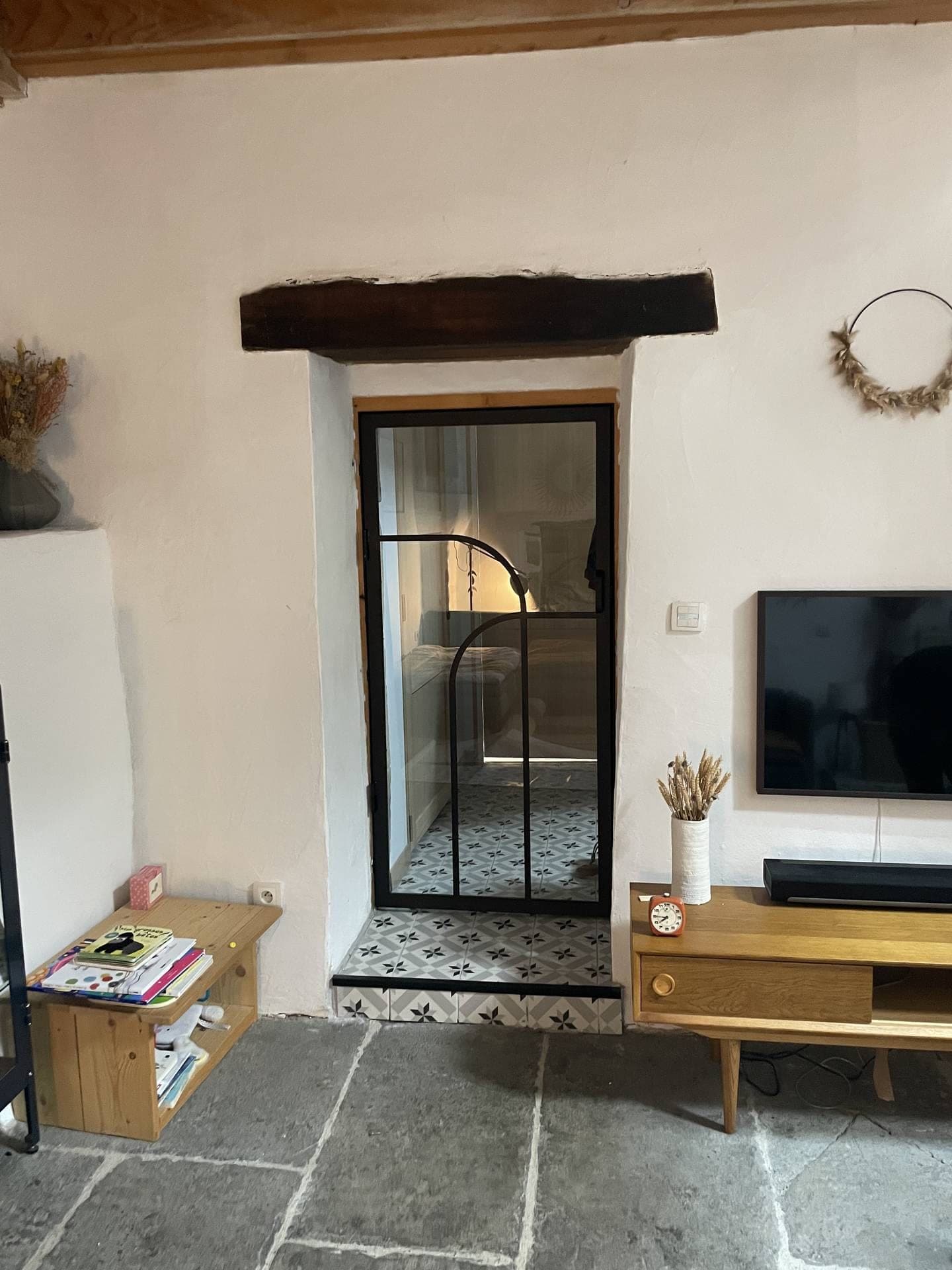 Porte verrière arrondie fermée dans une embrasure sous une poutre en bois, séjour au sol de dalles de pierre