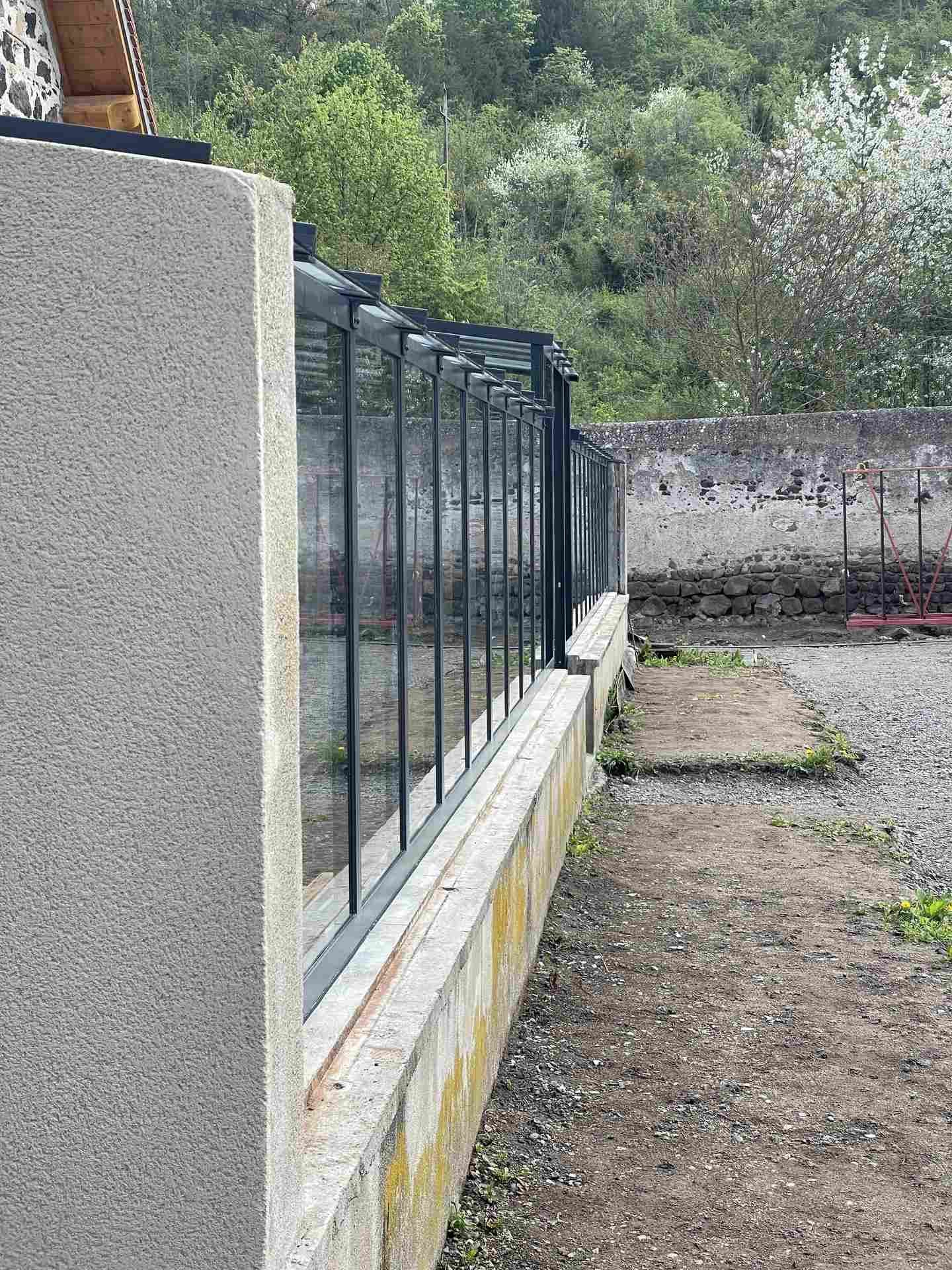 Détail des montants d’acier et du vitrage de la serre, posés sur le muret maçonné
