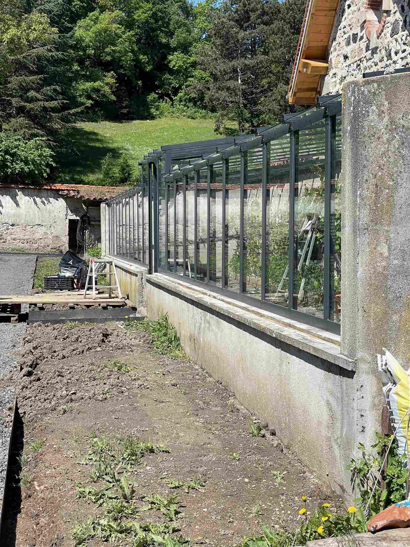 Enfilade de la serre vue depuis son extrémité, chevrons d’acier en débord et plantations palissées à l’intérieur