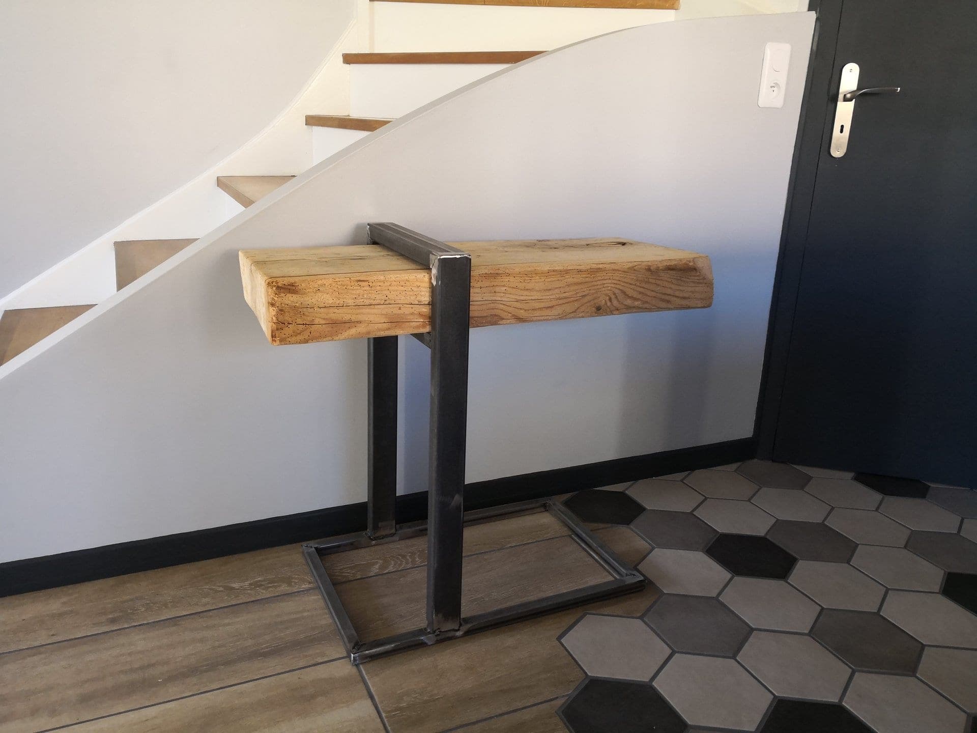 Table d’appoint : poutre ancienne tenue par un cadre en acier brut, devant un escalier