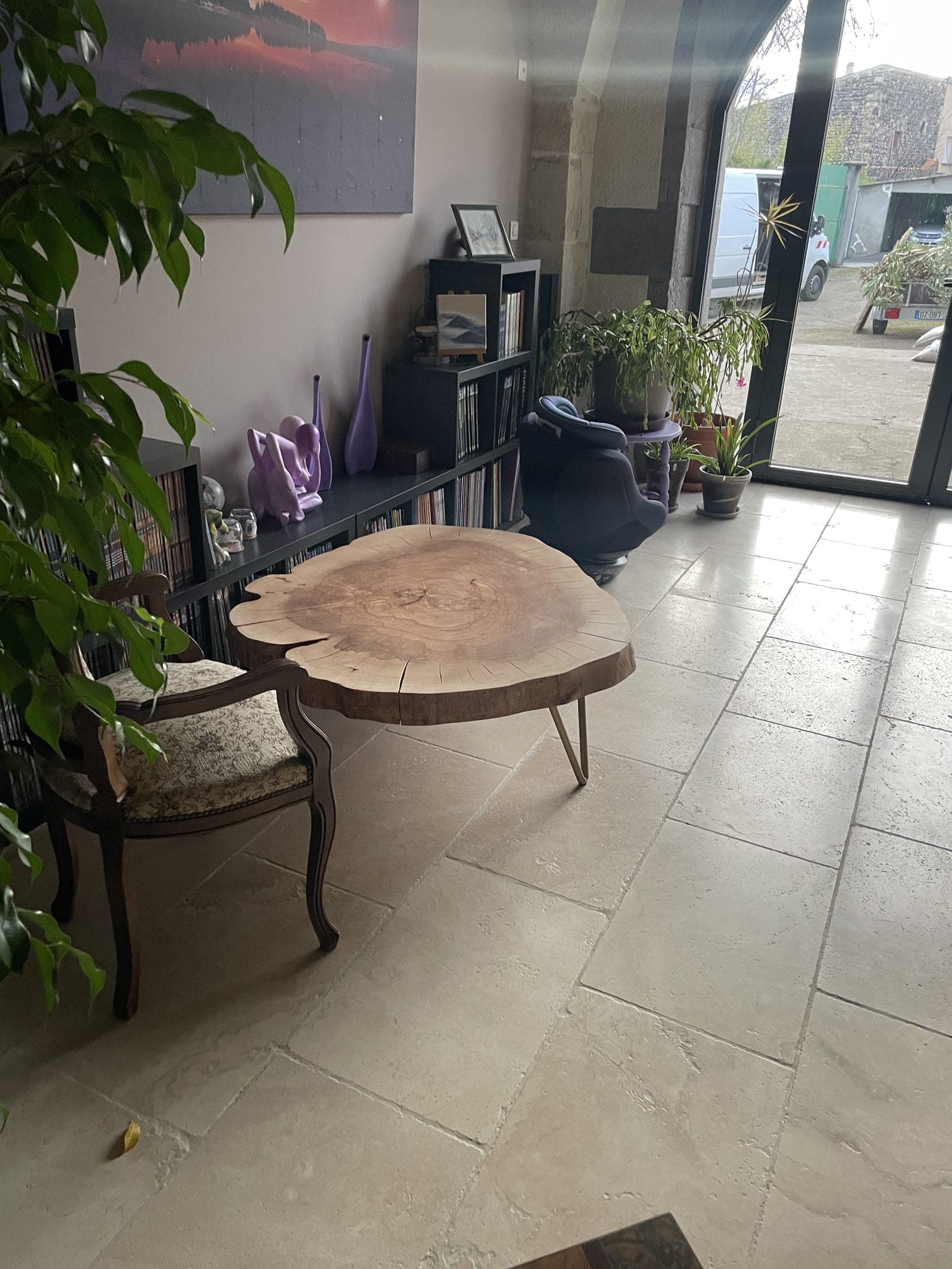 Table basse en tranche de hêtre dans un intérieur, devant une bibliothèque et une baie vitrée