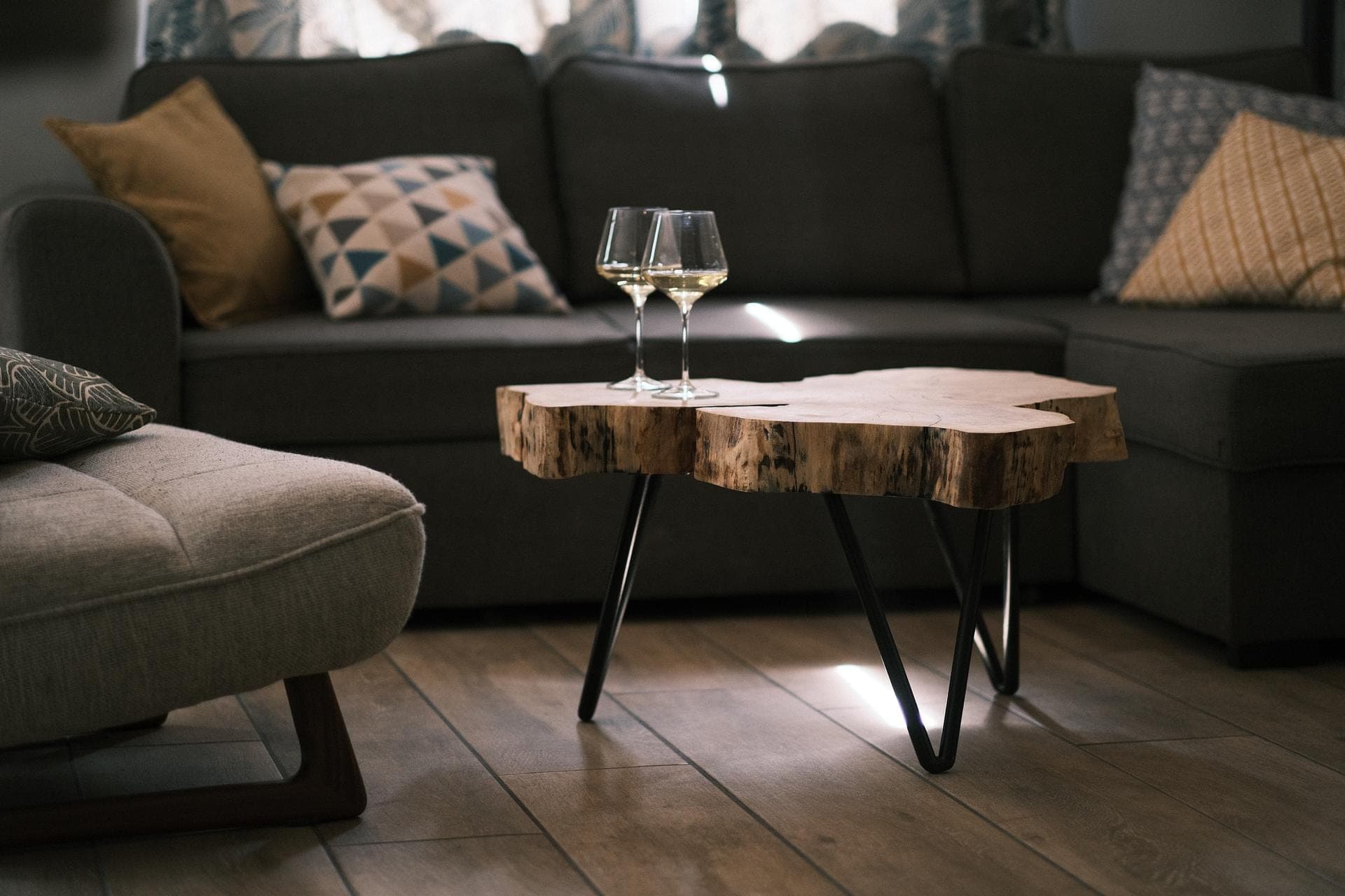 Table basse en tranche de peuplier sur pieds épingle noirs devant un canapé gris, deux verres posés dessus
