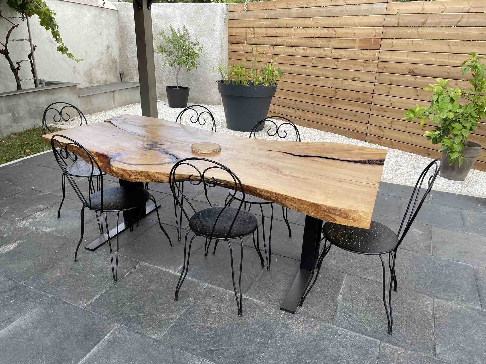 Table en tilleul massif à bords naturels sur pieds en acier noir, six chaises autour, sur une terrasse