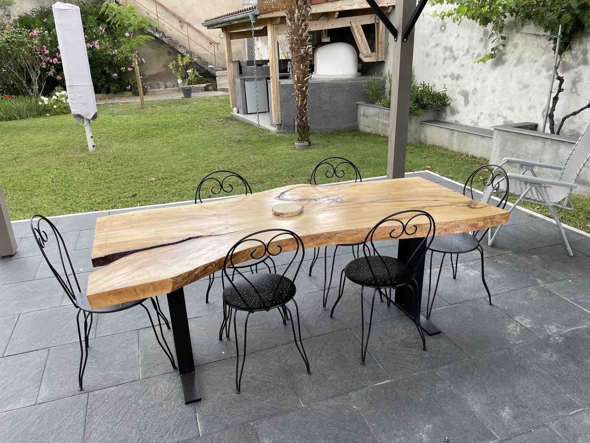 Table en tilleul massif vue en plongée, plateau au contour irrégulier, six chaises, jardin en arrière-plan