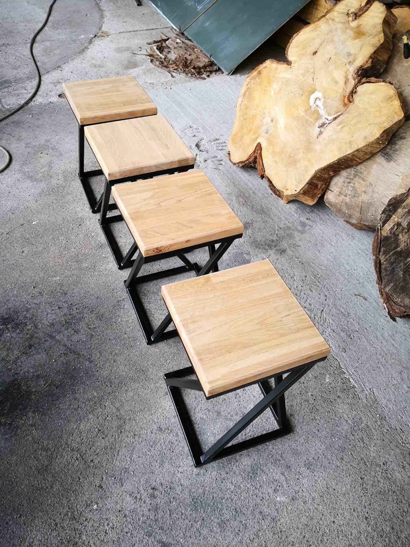 Quatre tabourets à pieds croisés alignés au sol, à côté de tranches de tronc