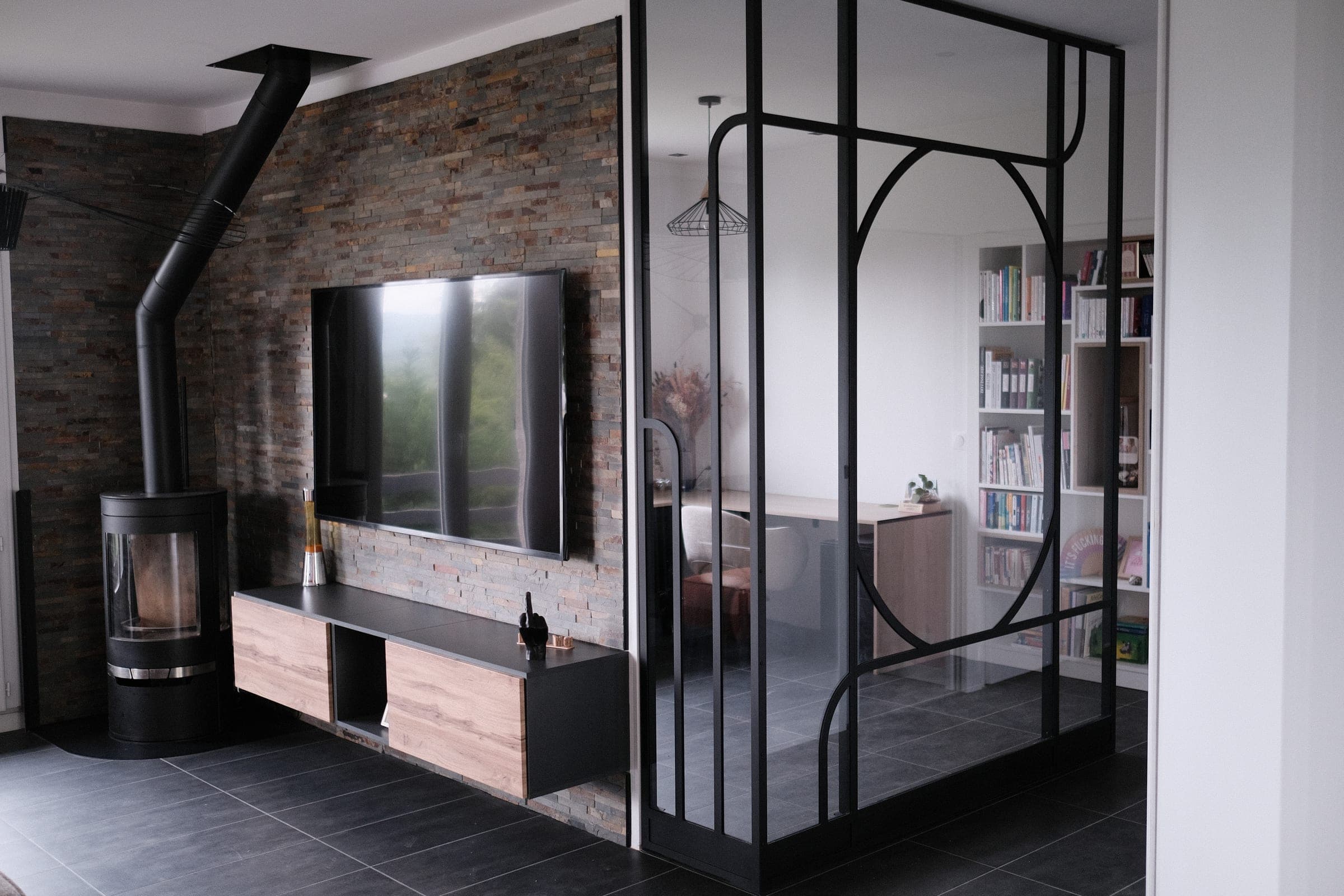 Verrière Art déco noire en angle, du sol au plafond, entre un séjour avec poêle et un bureau-bibliothèque