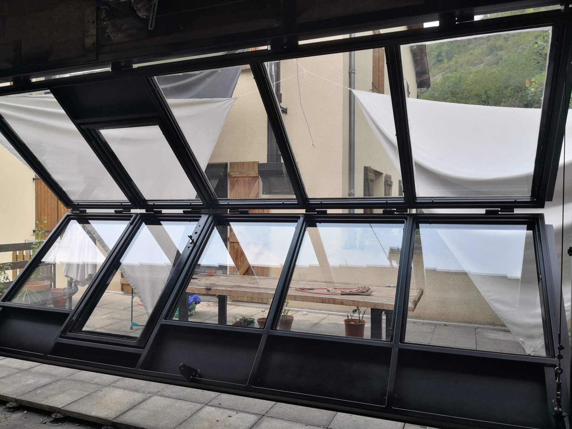 Verrière ouverte vue de l’intérieur, sections vitrées repliées au-dessus de la terrasse.