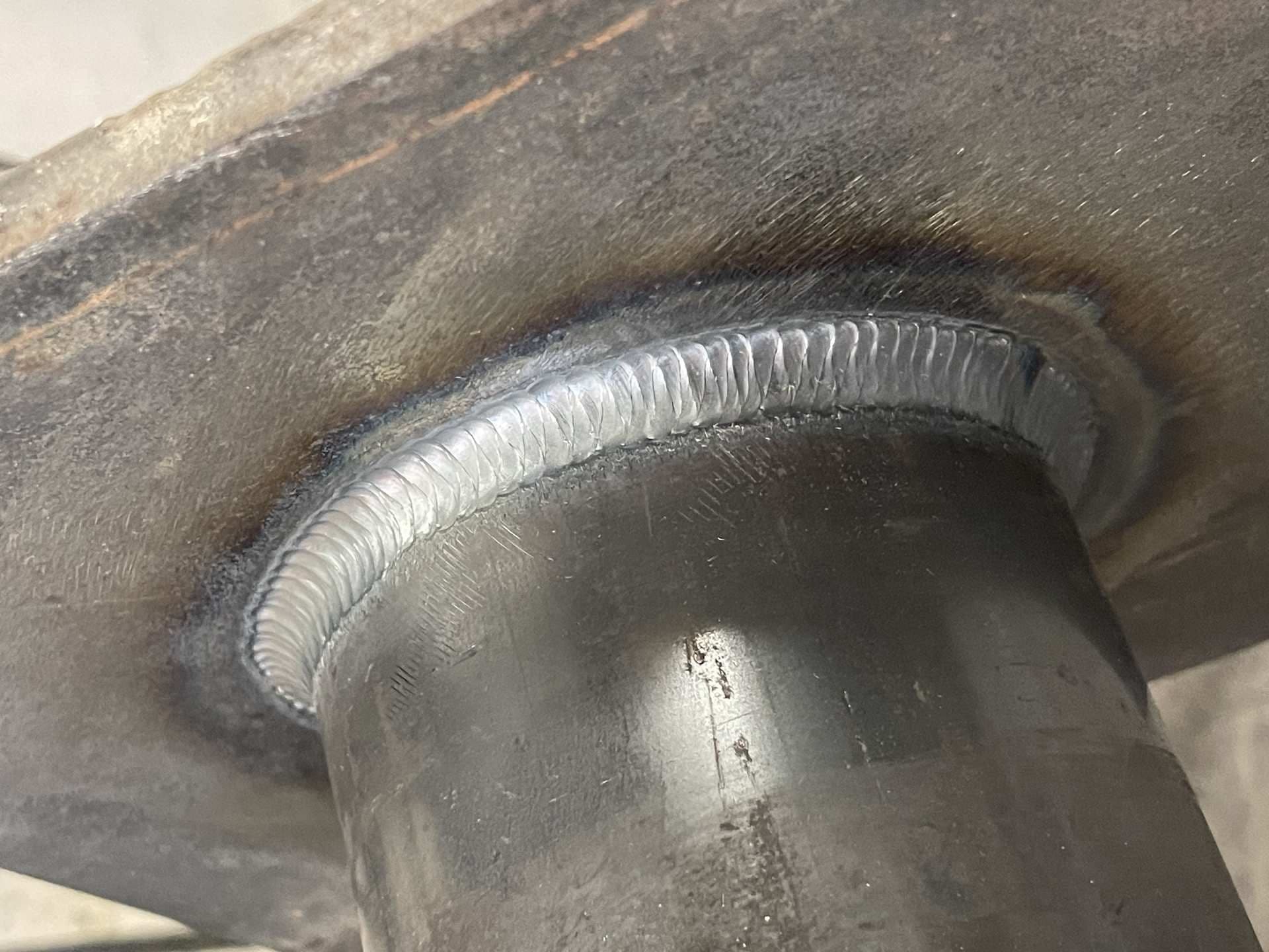 Gros plan d’un cordon de soudure TIG régulier entre un tube et une platine en acier.